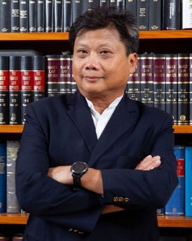 Legal professional standing confidently with arms crossed in front of law books.